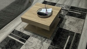 Un salon moderne avec un canapé gris, une table basse en bois surmontée d’un plateau, et un tapis à motifs.