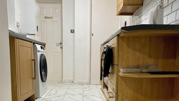 Une cuisine équipée d’un lave-linge, de meubles en bois et d’un sol carrelé.