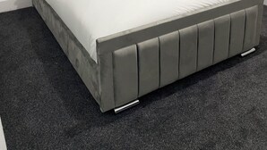 Un lit moderne avec une tête de lit rembourrée de couleur grise, une literie blanche et une serviette enroulée posée sur le lit.
