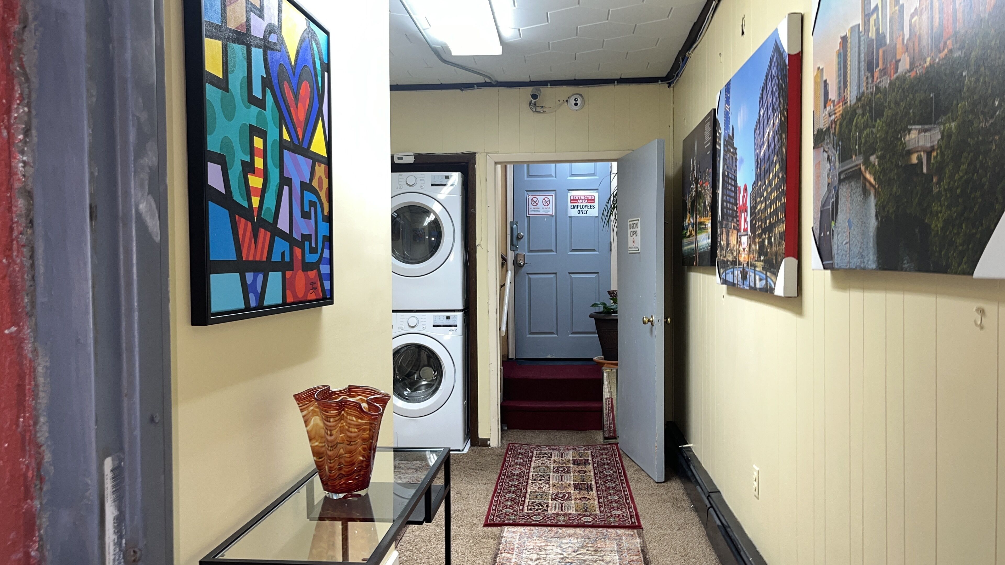 A hallway with a washing machine, a door marked "Employees Only," and a cityscape poster.