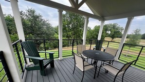 A covered outdoor deck with a table and chairs, surrounded by a metal railing and a view of a grassy area. - Camp Landa Resort (New Braunfels)
