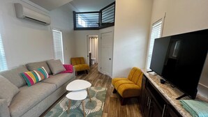 A compact living space with a sofa, a small table, a yellow armchair, a television, and a staircase leading to an upper level. - Camp Landa Resort (New Braunfels)