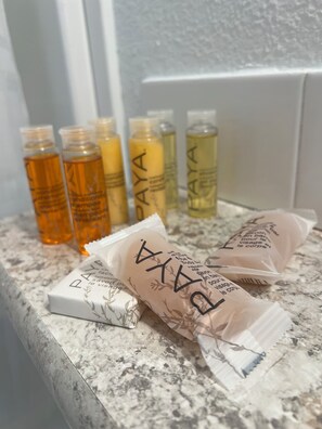 A bathroom counter with various bottles of shampoo and conditioner, some in plastic packaging. - Camp Landa Resort (New Braunfels)