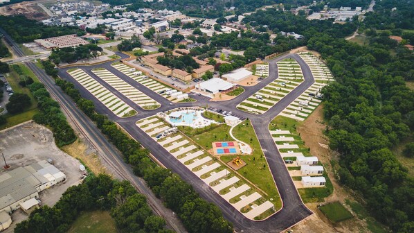 Vue aérienne d’un terrain de camping comprenant plusieurs aires de stationnement pour véhicules récréatifs, une piscine centrale et une végétation luxuriante tout autour.