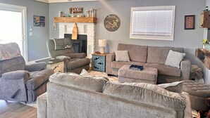 A living room with a fireplace, a ceiling fan, and a large window with blinds. - Kentucky Lodge | Blue Branch | Lake of the Ozarks (Tom Township)