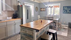A modern kitchen with a central island, stainless steel appliances, and a dining area with a view of the outdoors. - Kentucky Lodge | Blue Branch | Lake of the Ozarks (Tom Township)