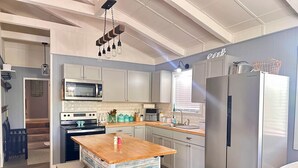 A modern kitchen with a central island, bar stools, a stainless steel refrigerator, and a microwave. - Kentucky Lodge | Blue Branch | Lake of the Ozarks (Tom Township)