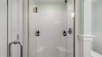A glass-enclosed shower with a white tiled wall and a white toilet visible to the right.