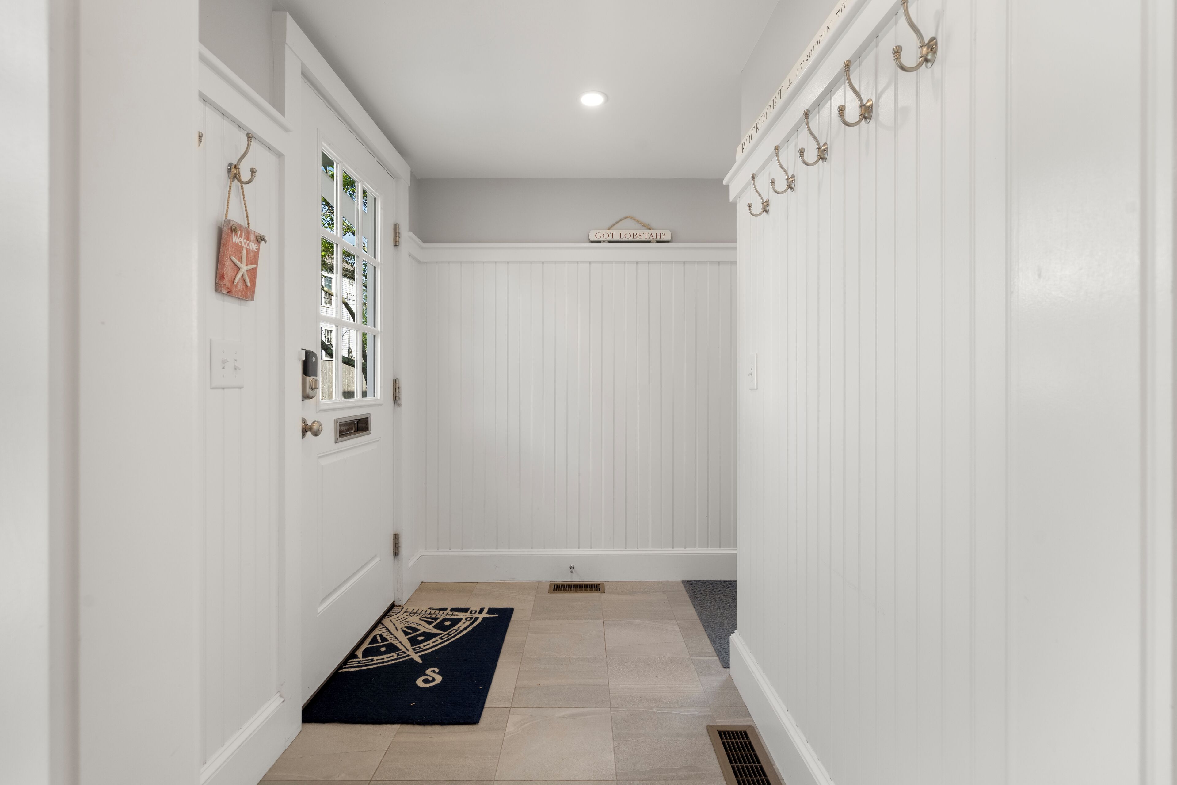 A hallway with white walls, a dark blue rug, and a sign above the door.