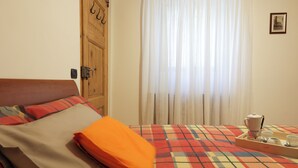 Habitación de hotel con cama, puerta de madera, ventana con cortinas y una bandeja con cafetera y tazas.