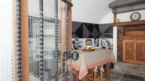 Un comedor con una mesa dispuesta para dos, una puerta de madera con un picaporte de metal, y una pared con un diseño geométrico y un reloj.