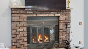 Ein moderner Kamin mit Ziegelverkleidung, ein Flachbildfernseher darüber und ein Glastisch davor.