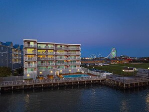 Un hotel de varios pisos con balcones, piscina y un embarcadero que se adentra en el agua.