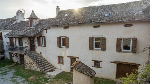 Un edificio de piedra tradicional con techo inclinado, contraventanas de madera y un pequeño balcón con mobiliario exterior.