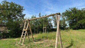 Un columpio de madera en un área cubierta de césped, con árboles al fondo.