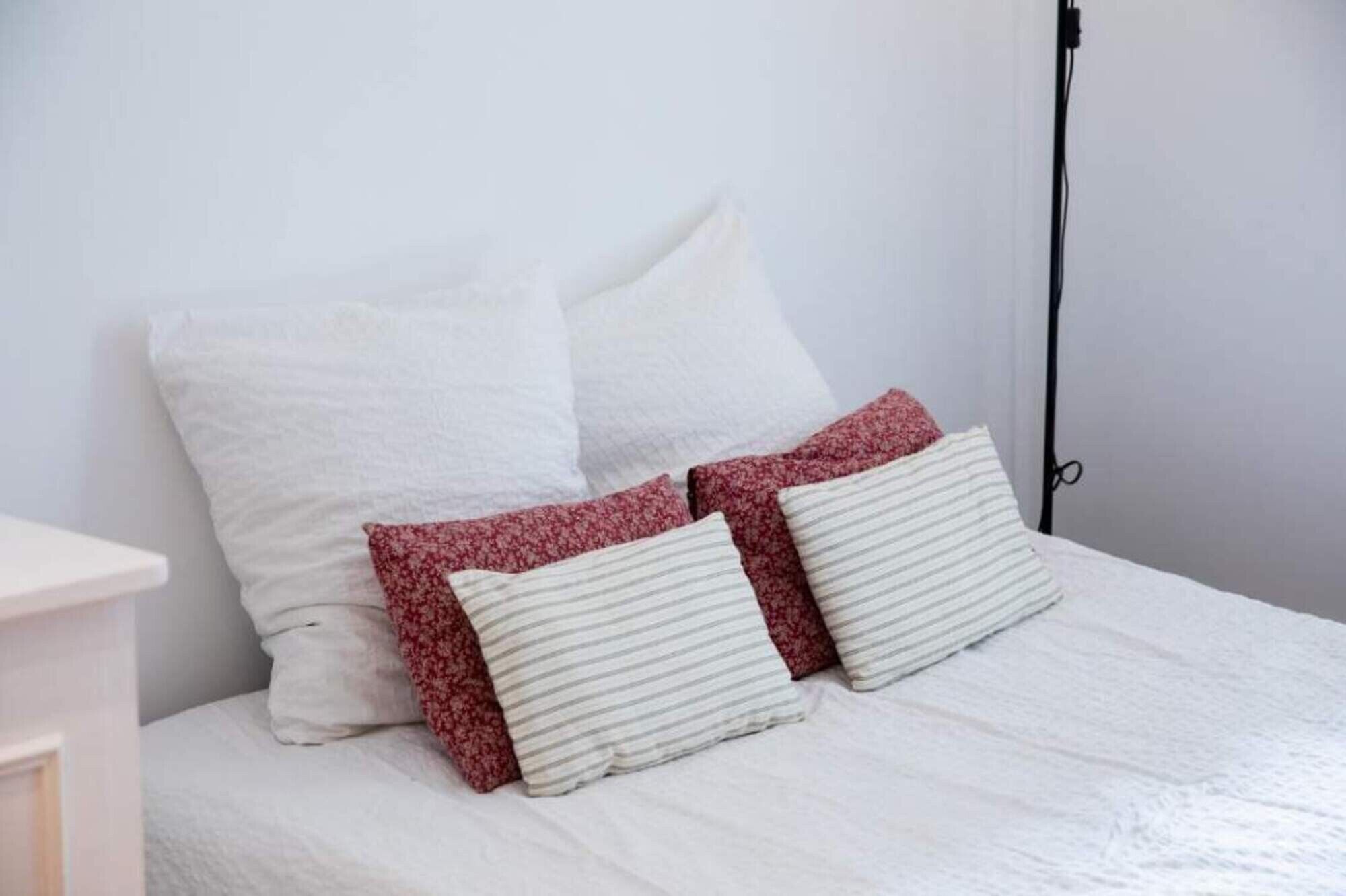 A bed with white bedding and two pillows, one with a floral pattern and the other striped.