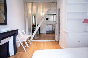 Une chambre à coucher avec un lit, un bureau et une chaise. Un escalier mène à un espace cuisine.
