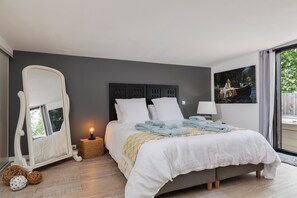 Quarto com cama, espelho, mesa de cabeceira, abajur e um quadro na parede.