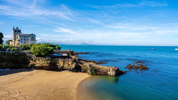 A coastal hotel with a beach, clear blue waters, and a mountainous backdrop. - Apartment 'Residence Le Sabaou' with Balcony (Biarritz)