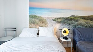 A bedroom with a bed, a small bedside table with a lamp, and a wall mural of a beach. - Apartment 'Residence Le Sabaou' with Balcony (Biarritz)