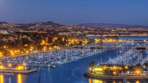 Un port de plaisance où sont amarrés de nombreux bateaux, entouré d’un paysage urbain avec des bâtiments illuminés au crépuscule.