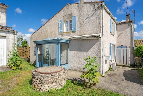A two-story house with a stone foundation, a blue door, and a small garden area.