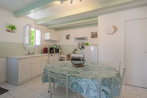 A kitchen with white cabinets, a dining table with a leaf-patterned tablecloth, a white refrigerator, and a clock on the wall.