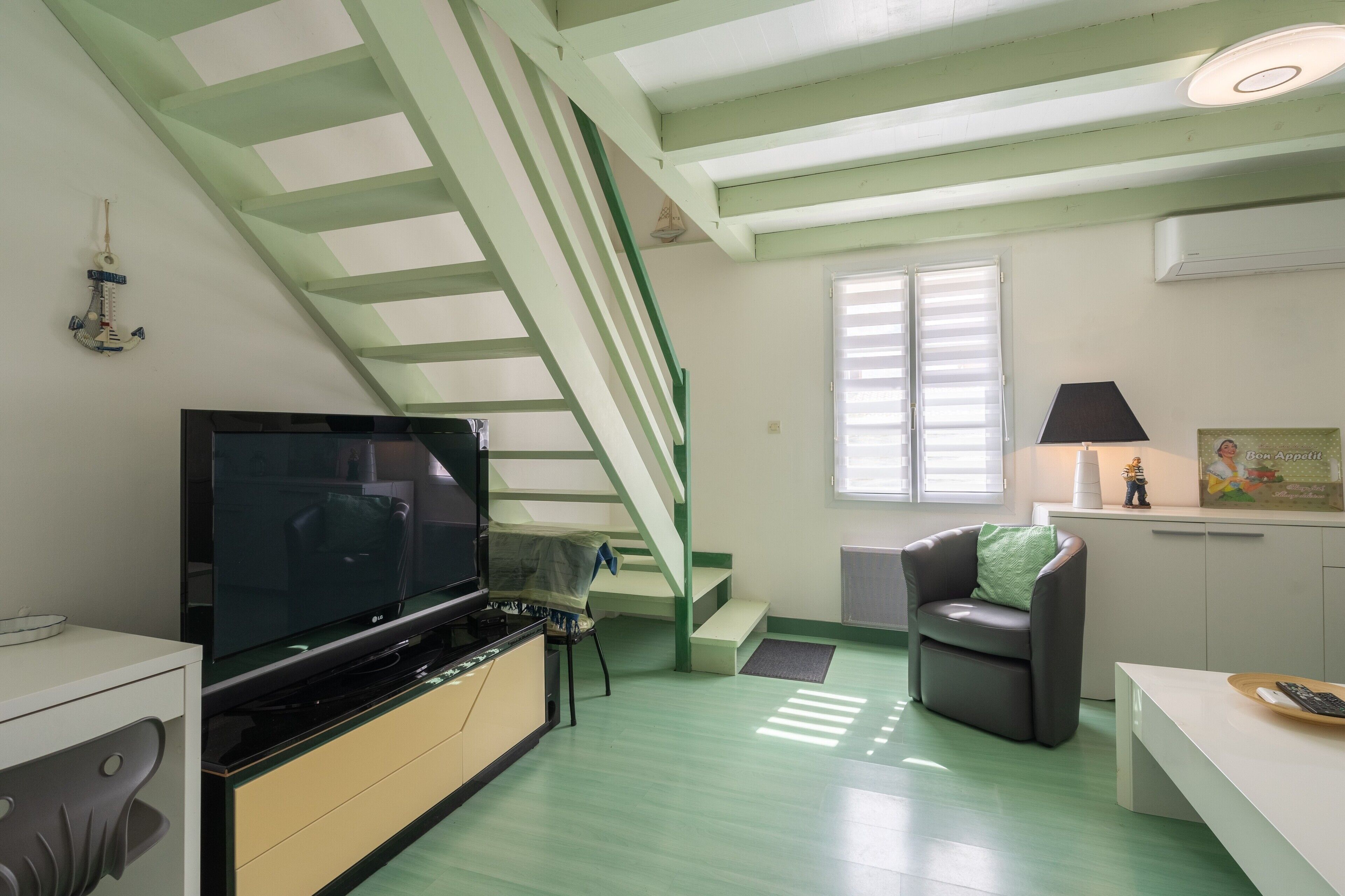 A modern kitchen with a TV, a staircase, and a dining area.