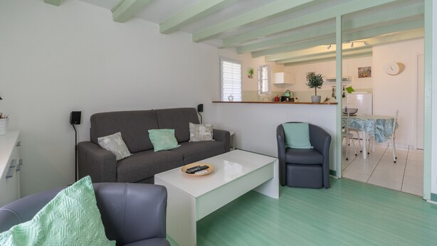 Een moderne woonkamer met een bank, een salontafel en een stoel. Een keuken is zichtbaar door een open doorgang.