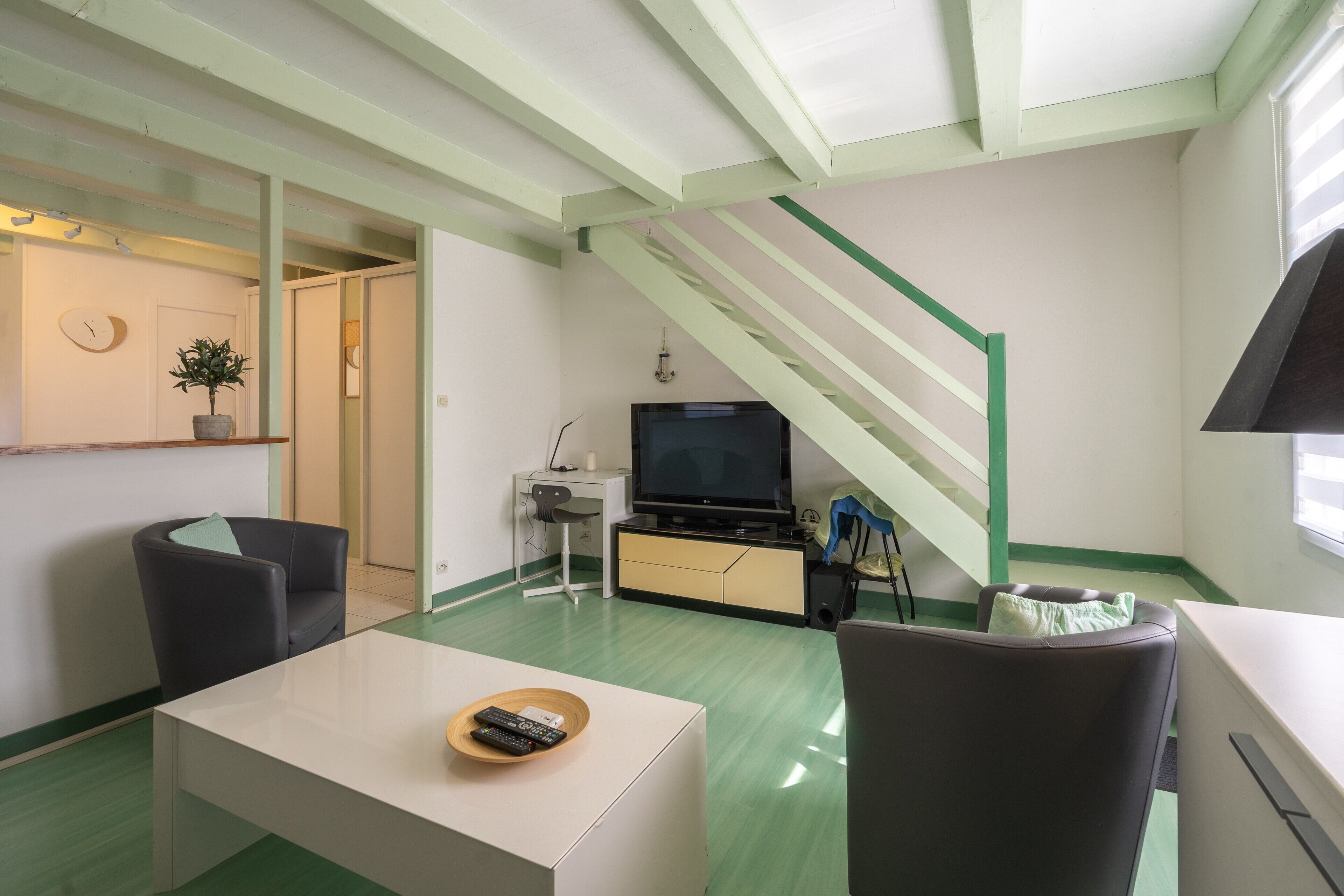 A living room with a television, a sofa, a coffee table, and a staircase.