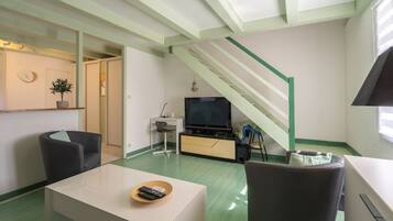A living room with a television, a sofa, a coffee table, and a staircase.