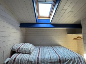 Een kleine kamer met een enkel bed, schuine kap en dakraam, met een bedovertrek met dessin en een houten wand.