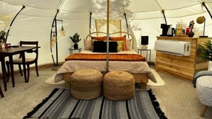 A tent with a bed, bedside table, lamp, and a small wooden dresser.