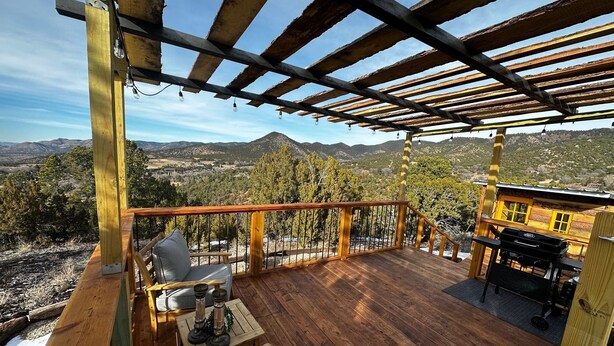 A wooden deck with a view of mountains, a grill, and a seating area with cushions and a table.