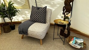A cozy room with a single sofa, a small table with decorative items, a potted plant, and a tent-like structure in the background.