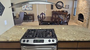 A kitchen with a gas stove, oven, granite countertop, dining area with a wooden table and chairs, and a stone fireplace. - Clean, Comfortable Home Away From Home! (El Paso)