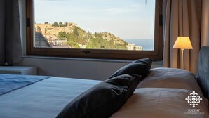 A hotel room with a large window offering a view of a historic hilltop city. - Casa Majorana - Vista mare (Taormina)