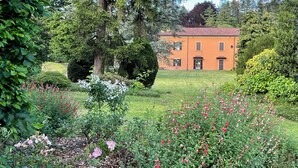 Ein Garten mit verschiedenen Pflanzen und Blumen, einer Rasenfläche und einem Gebäude mit rotem Dach.