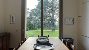 Ein Essbereich mit Tisch für zwei Personen, Blick auf einen Garten durch ein großes Fenster und eine Kommode rechts.