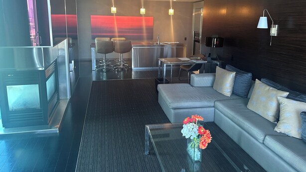 A modern hotel room with a sofa, a glass coffee table with flowers, a dining area with a table and chairs, and a kitchen area. - 1220 square feet strip view with upgraded WiFi  (Las Vegas)