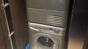 A compact, stainless steel, front-loading washing machine with a control panel, located in a small laundry room with a tiled floor. - 1220 square feet strip view with upgraded WiFi  (Las Vegas)