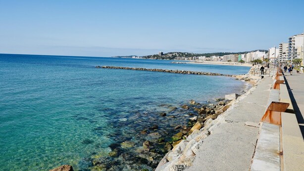 A coastal cityscape with clear blue waters, a rocky shoreline, and a promenade with buildings and people. - Mundet 1 Baix Mar CostaBravaSi - Sea, beach and AC (Sant Antoni de Calonge)
