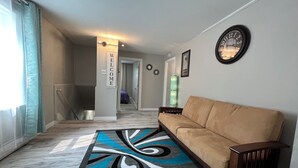 Una sala de estar moderna con un sofá color beige, una alfombra estampada y un reloj de pared.