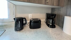 Una cocina con tostadora, cafetera y hervidor sobre una encimera de mármol.