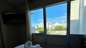 A hotel room with a bed, a rolled towel, and a window with a city view.