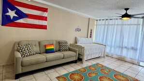 A living room with a sofa, a bed, a ceiling fan, a flag, and a patterned rug.