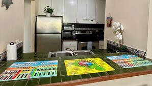 A kitchen with white cabinets, a stainless steel refrigerator, and a microwave. There are two black bar stools in front of the counter.
