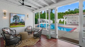 Un patio cubierto con sillas de mimbre, un cuadro y vista a una piscina.