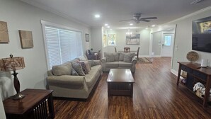 Olohuoneessa on sohva, sohvapöytä ja televisio. Huoneessa on myös kattotuuletin, ikkuna, jossa on sälekaihtimet, ja ovi, joka johtaa toiseen huoneeseen.