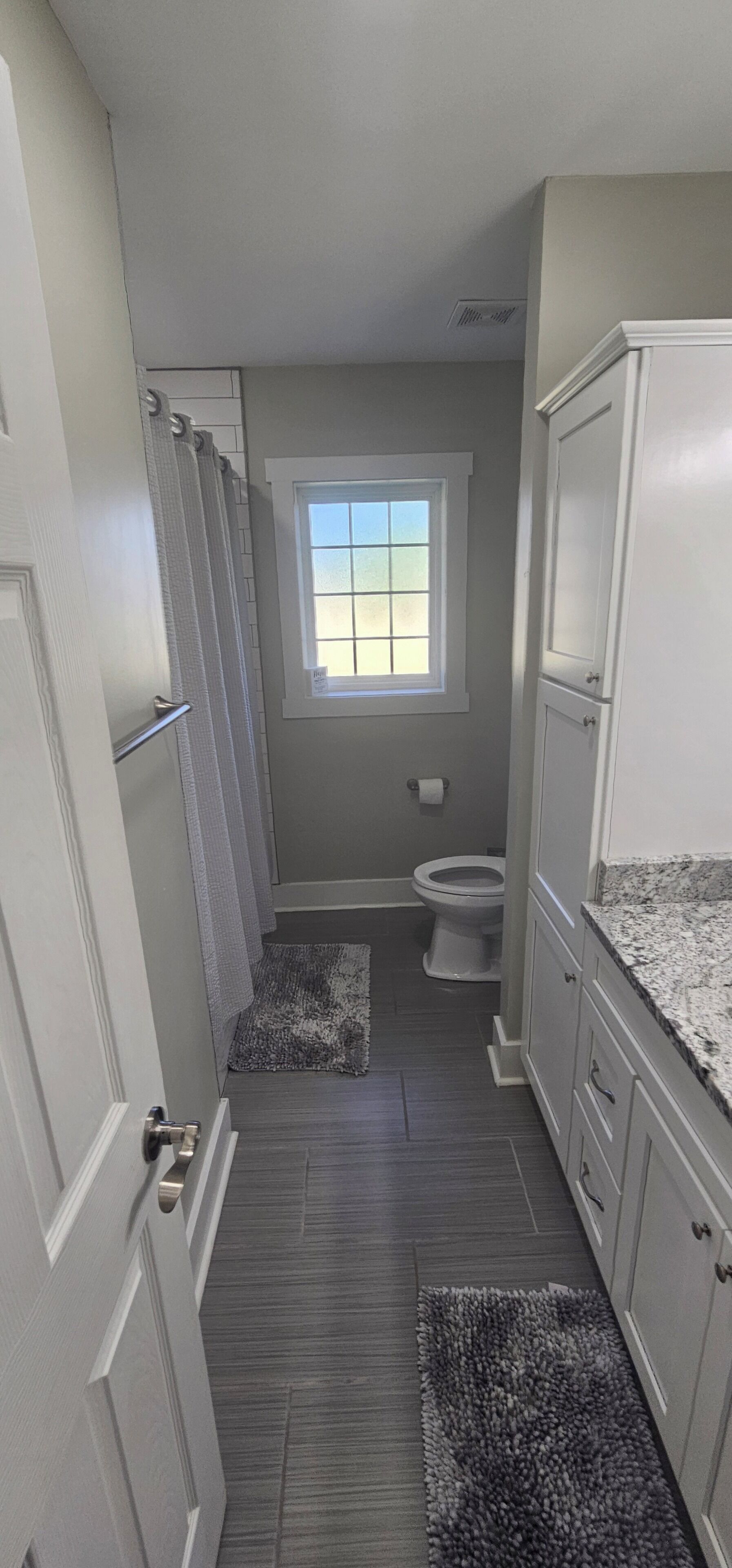 A narrow bathroom with a window, a toilet, and a shower area.